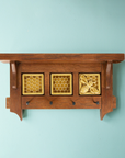 This triptych key rack features one Honey Bee Tile and two Honeycomb tiles. The Honeybee Tile features a large honeybee with stripes and detailed segmented wings sitting on a honeycomb patterned background. The Honeycomb tiles are a flat line-drawing of a honeycomb pattern with a simple smooth border around it. These three tiles are lined up and attached in a brown oak key-rack. The key-rack has a small shelf at the top and four black iron nails stick out of the bottom to hang your keys on.