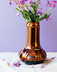 The Celtic Vase's base starts out wide and round at the bottom then becomes a straight pillar as it continues upward with a winding line design that has no beginning or end. The Copper iridescent glaze is a shiny, smooth metallic glaze with many variations. Some pieces end up with a blue-gray flashing of color that covers a portion of the surface.