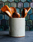 A textured ice-blue Frost glaze holding teakwood utensils with an Aurora Iridescent tile wall.