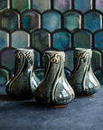 Three glossy, deep green Balsam Snowdrop vases against an Aurora Iridescent tile wall.