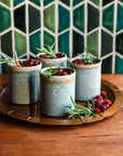 Five ceramic Rocks Cups with greenery and berries on a wooden tray against a geometric-patterned wall.