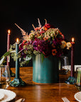 Floral arrangement in a freckled Greenstone vase on a wooden table with candles and glasses.