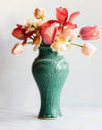 A Pewabic Green-glazed, Large Classic Vase dressed with pink tulips, and neutral daffodils against an ivory backdrop.