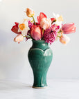 A Pewabic Green-glazed, Medium Classic Vase dressed with pink tulips, and neutral daffodils against an ivory backdrop.