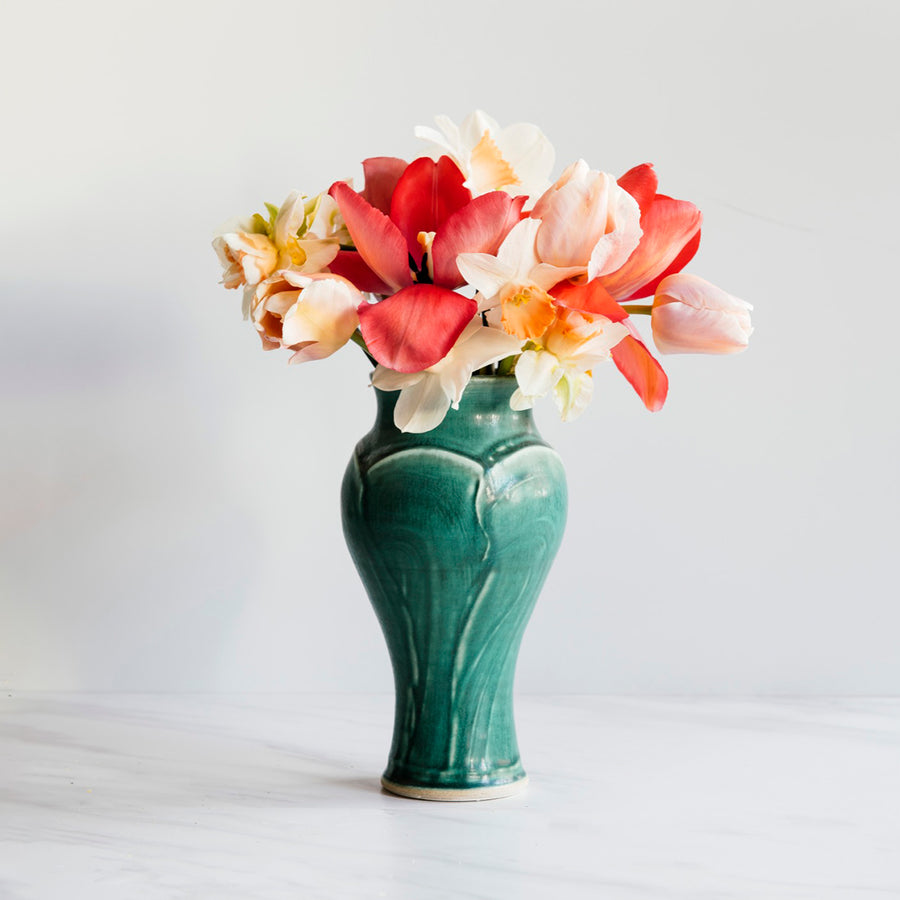 A Pewabic Green-glazed, Small Classic Vase dressed with pink tulips, and neutral daffodils against an ivory backdrop.