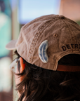 This Feather is pinned onto the back of a dusty mauve colored baseball cap.