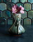 Glossy, deep green Balsam Snowdrop vase with purple hellebore flowers against an Aurora Iridescent tile wall.