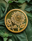 A two-tone glossy, round Sunflower Trivet with golden border and outline set against an emerald green background.