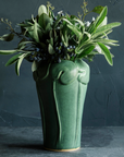 The Lotus Vase features a tall base with long stalks reaching up to a ring of lily pads that crown the top and lip of the vase.