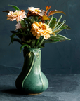 An Elm-glazed ceramic Snowdrop Vase, containing a bouquet of muted peach flowers and sage on a dark background.