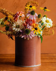 This Crock features the matte brownish-red tones of the Cinnamon glaze. Sitting on a wooden table, this crock is used as a vase, holding black eyed susans, dahlias and other end of summer blooms.