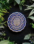 A Mooncake Paperweight in two-tone Lapis/Scrape surrounded cool greenery and delicate concord grapes.