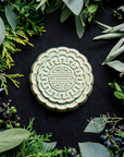 A Mooncake Paperweight in our glossy Celadon glaze, surrounded by cool greenery and delicate concord grapes.