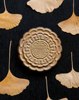 A Mooncake Paperweight in shimmering Blush Iridescent surrounded by dried ginkgo leaves.
