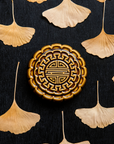 A Mooncake Paperweight in our glossy Molasses glaze, surrounded by dried ginkgo leaves.
