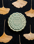 A Mooncake Paperweight in our glossy Celadon glaze, surrounded by dried ginkgo leaves.