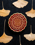 A Mooncake Paperweight in two-tone Scarlet/Honey surrounded by dried ginkgo leaves.