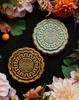 Two Mooncake Paperweights in glossy Celadon and Molasses glaze surrounded by bright, summer florals and gooseberries.