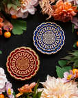 Two Mooncake Paperweights in two-tone Lapis/Scrape and Scarlet/Honey surrounded by vibrant summer flowers and gooseberries.