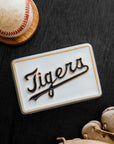 Baseball, baseball glove, and 'Tigers' logo tile on a dark wood surface.
