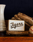Baseball glove, baseball, Pewabic Step Vase in a Birch glaze, and a 4x6 'Tigers' tile on a wooden shelf.