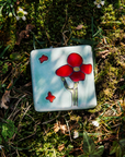 The handpainted tile in the Poppy Palette features bight red petals and a medium green cactus stem. The background of the tile is a pale blue color.
