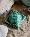 This thick high relief paperweight has the shape of a small turtle. It has detailed feet, face, and shell and sits on a square base.