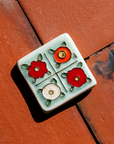 The Four Flowers Tile is segmented into four sections, each section has one flower inside it. The flowers have yellow centers and either red, deep orange or white petals.