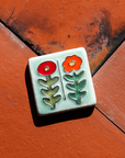 The Two Flowers Tile features two flowers on long, straight, leafy stems. One flower has scalloped petals while the other is circular.