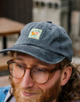 Man wearing a dark gray cap with a square colorful floral patch in the pottery courtyard.