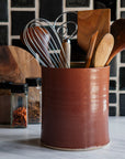 This Cinnamon glazed Crock sits in a modern black and white kitchen, holding wooden and metal cooking utensils.