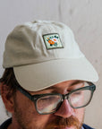 A man wears the off-white version of the Floral Tile Hat. The colorful, square patch is embroidered onto the muted white baseball cap.