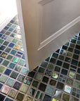 A blend of blue and green tiles in a range of textures and glazes on the floor at the  entryway of a home. The door is slightly ajar, welcoming you into the space.