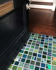 A blend of blue and green tiles in a range of textures and glazes on the floor at the  entryway of a home. The door is slightly ajar, welcoming you into the space.