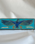 The short and wide Nekhbet tile features a line drawing of a vulture with wings outstretched, head turned to the right as she holds two stylized feathers- one in each talon. This tile features bright shades of blue.