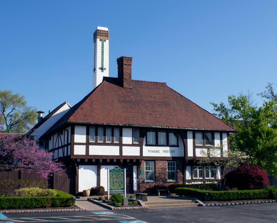 The historic Pewabic pottery building exterior has white stucco walls bordered by brown wooden beams and a terracotta tile roof. Its tall white chimney features colorful Pewabic tiles.