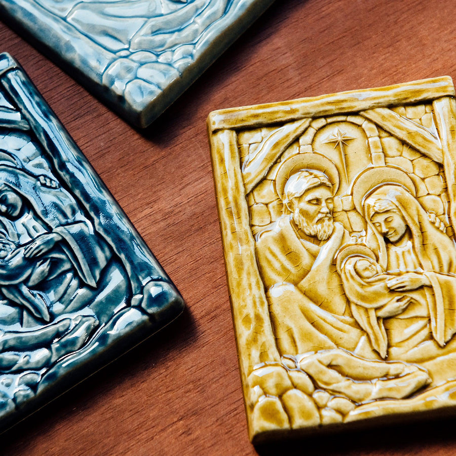 The Nativity Tile features the haloed holy family - Joseph, Mary and Baby Jesus - embracing under the wooden beams of the stable. Behind them, a window in the stone wall gives a glimpse of the Bethlehem star.