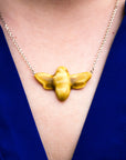Close up photo of a woman wearing our historically inspired ceramic Bee Necklace in a matte Mustard glaze with a royal blue blouse.