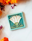 The Hand Painted Egyptian Lotus Tile features a line drawing of a white flower with four decorative shapes at the base - creating an Egyptian motif.