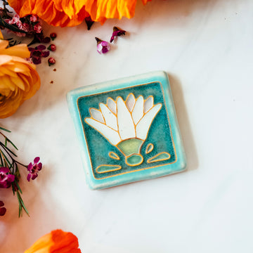 The Hand Painted Egyptian Lotus Tile features a line drawing of a white flower with four decorative shapes at the base - creating an Egyptian motif.