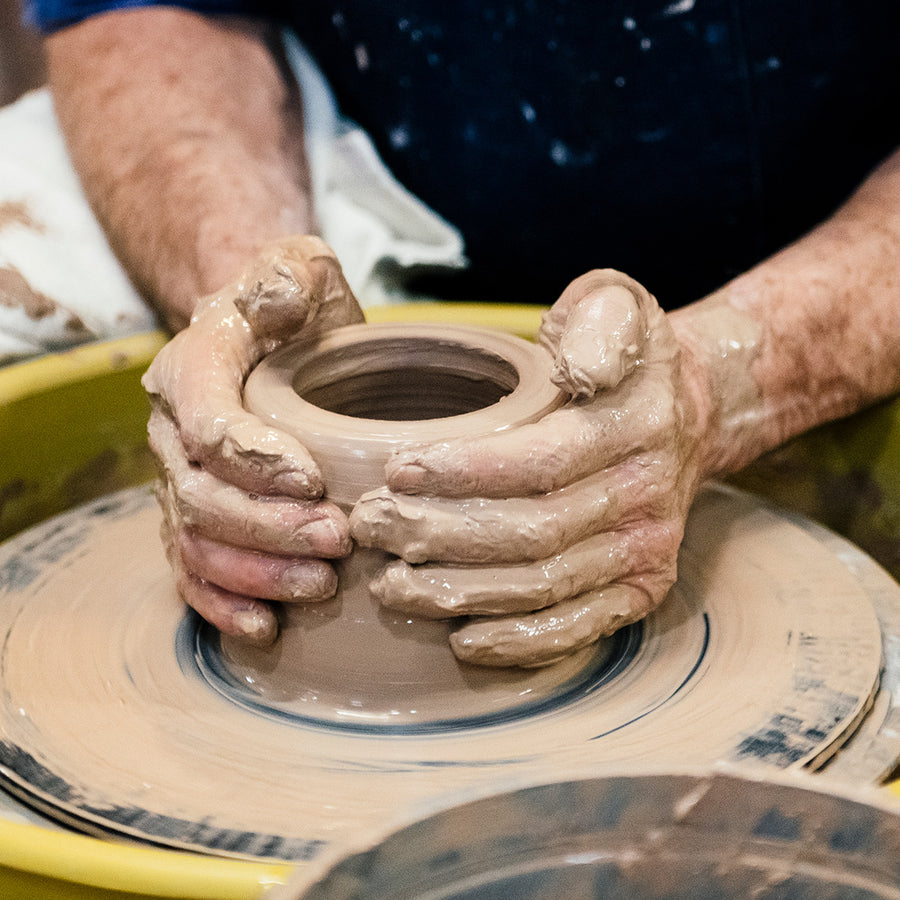 Hands mold wet clay into a cup shape on a pottery wheel.