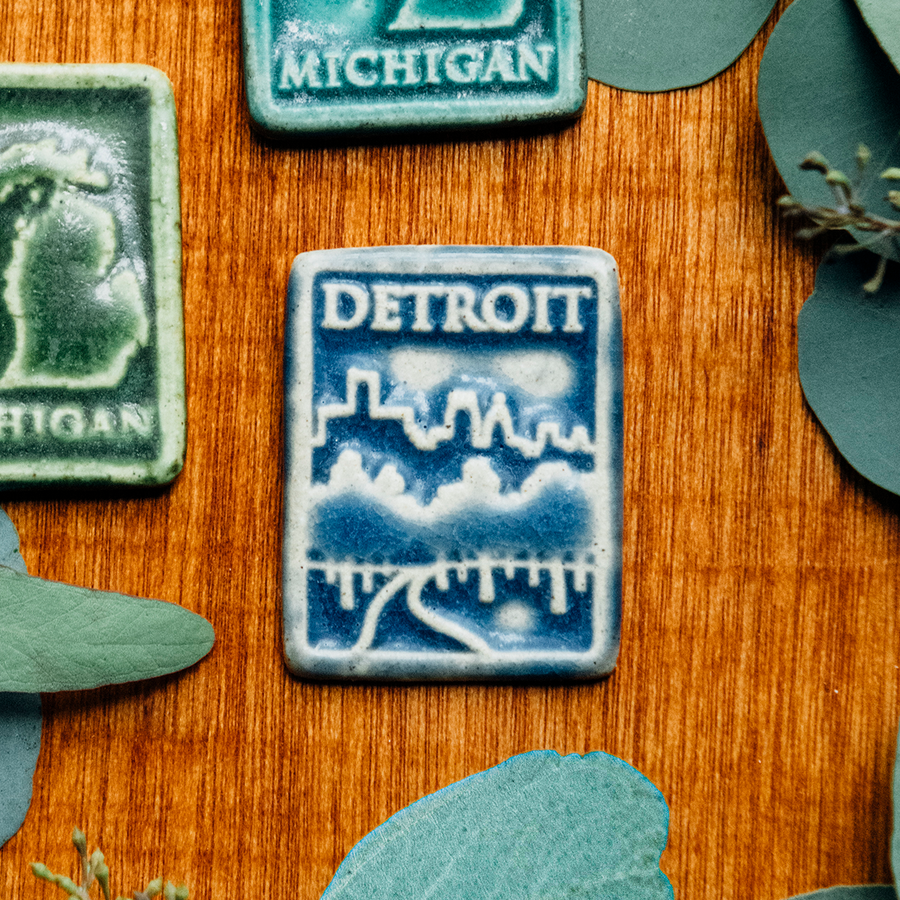 The Detroit Magnet is a rectangular tile featuring a tree lined road leading towards the Detroit skyline. The word Detroit is in bold letters across the top of the tile.