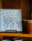 On the same wooden collector's shelves rests another Aztec Lion tile. This version features the gray-blue semi-gloss Dusk glaze. The lion faces the left.