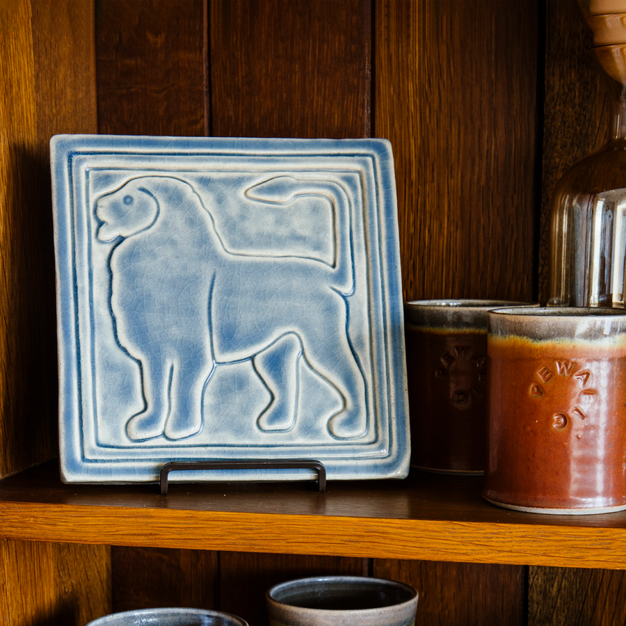 On the same wooden collector's shelves rests another Aztec Lion tile. This version features the gray-blue semi-gloss Dusk glaze. The lion faces the left.