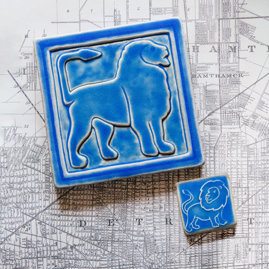 The Lion Tile featuring the Sky blue glaze sits next to a eight inch by eight inch right-facing Aztec Lion tile in the same glaze on a black and white map of Detroit. 