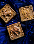 The Gemini tile lies with the other two Pewabic Zodiac tiles on rich, velvety fabric the color of the night sky. The Taurus tile features a sturdy bull with its head bowed and horns lowered. The Aries tile has an alert ram with its legs positioned as if it is prancing. The ram's head is turned backwards over its shoulder.