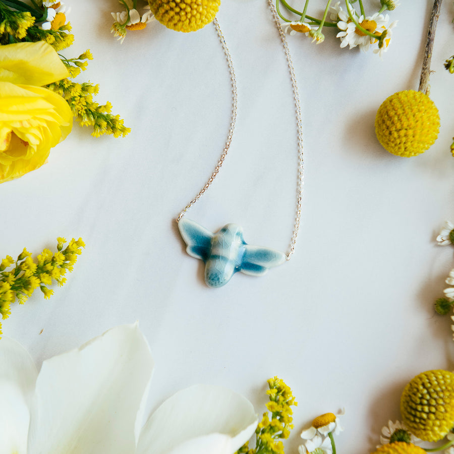 The blue Glacier Gloss glazed bee pendant is attached to a silver chain.