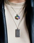 A person wears the Detroit Map Necklace and a Hex Necklace. They have a cream colored t-shirt and a black leather jacket.