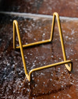 Detail photo of the matte gold tile stand. It is empty and on a tiled-window ledge.