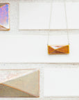 This necklace is resting next to the larger version of the pyramid design tile on the 2018 expansion of the Pewabic tile studio.
